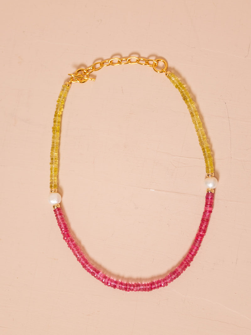 Necklace with pearls and yellow and pink beads against pink background.