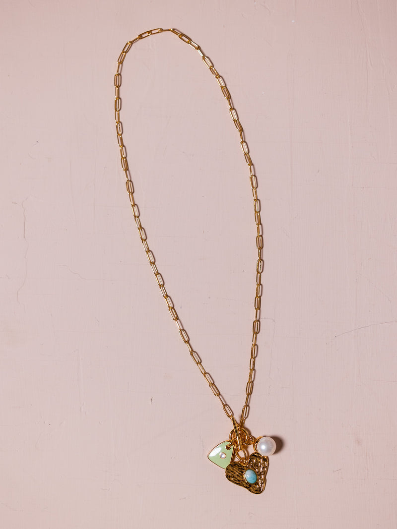 Gold necklace with multiple charms against pink background.