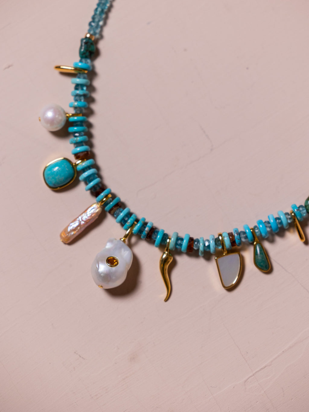 Necklace with blue beads and other charms against pink background.
