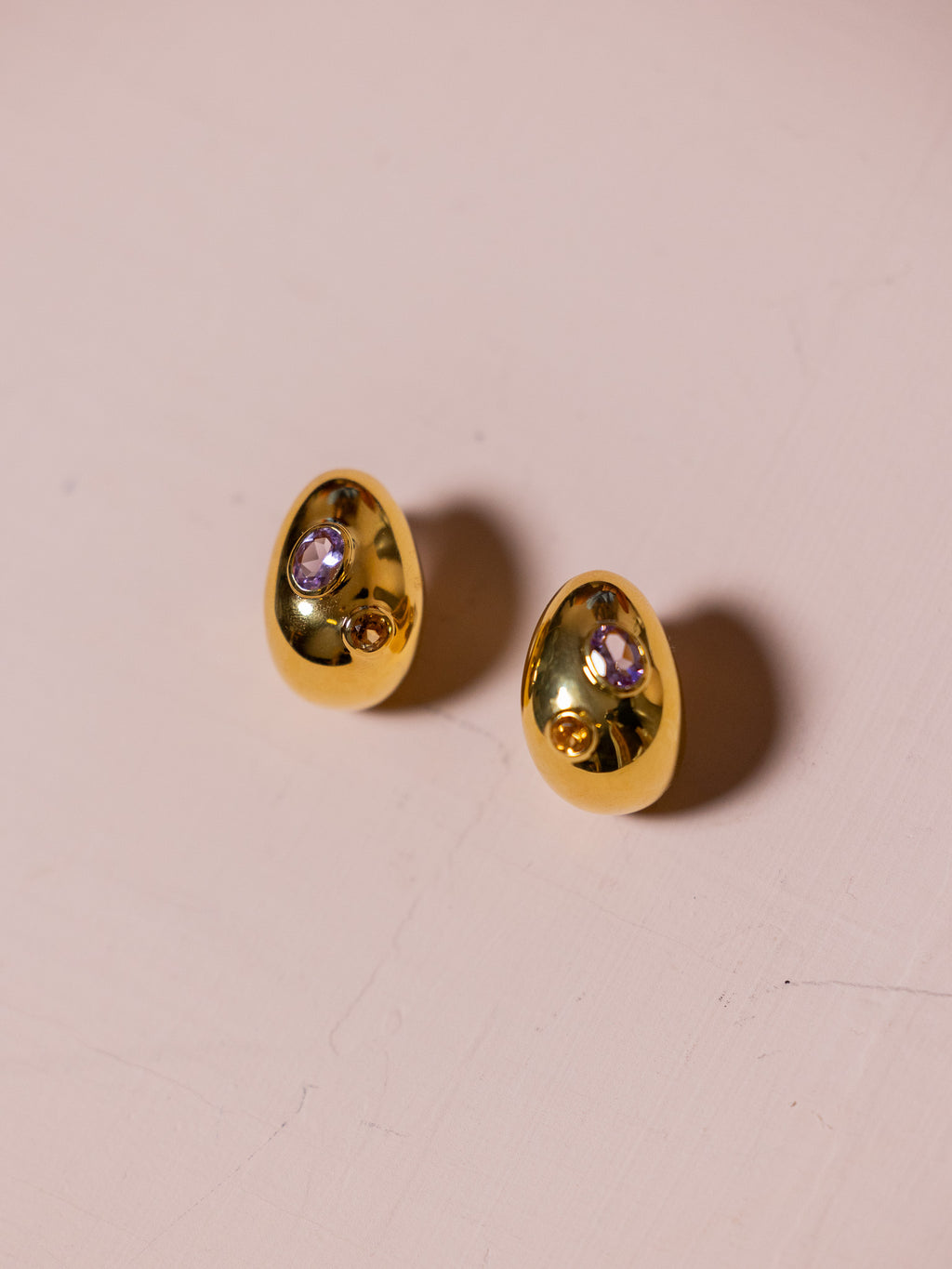 Gold earrings with inlaid jewels against pink background.