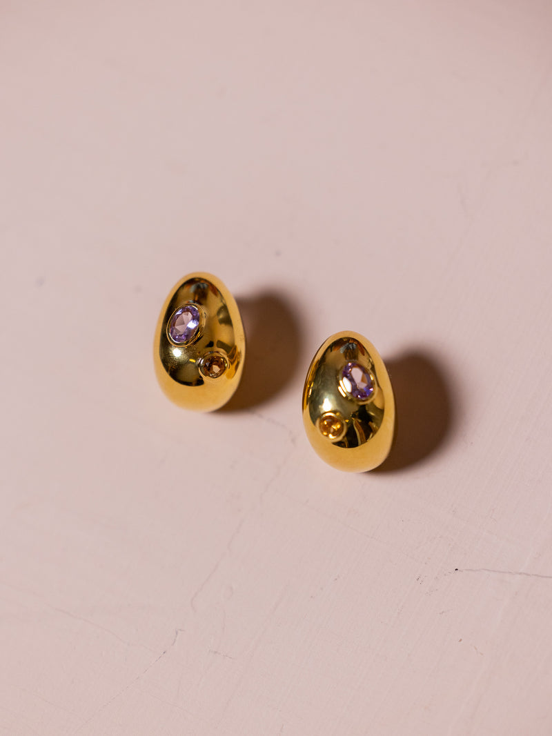 Gold earrings with inlaid jewels against pink background.