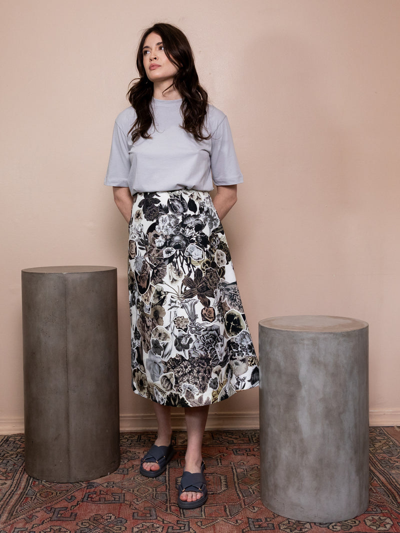 Woman wearing gray shirt and black and white floral collage skirt against pink background.