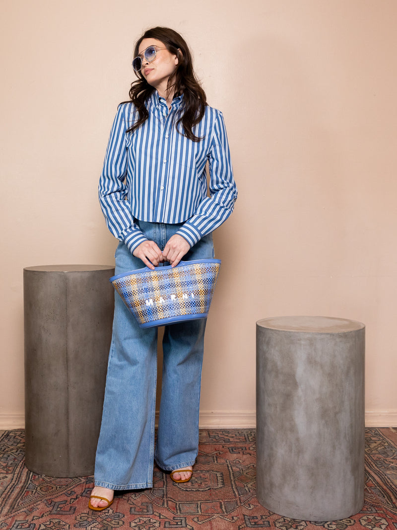 Woman in striped blue shirt and blue jeans holding a plaid bag against pink background