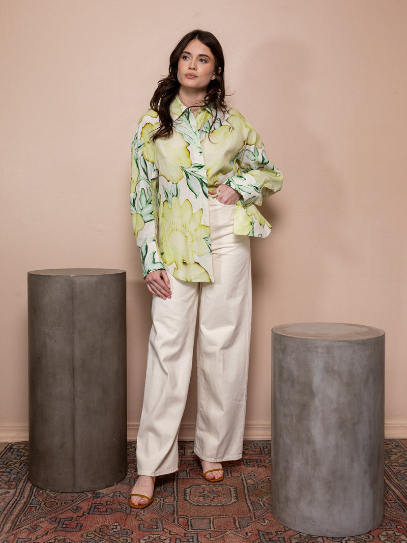 Woman wearing green floral top and white pants against pink background