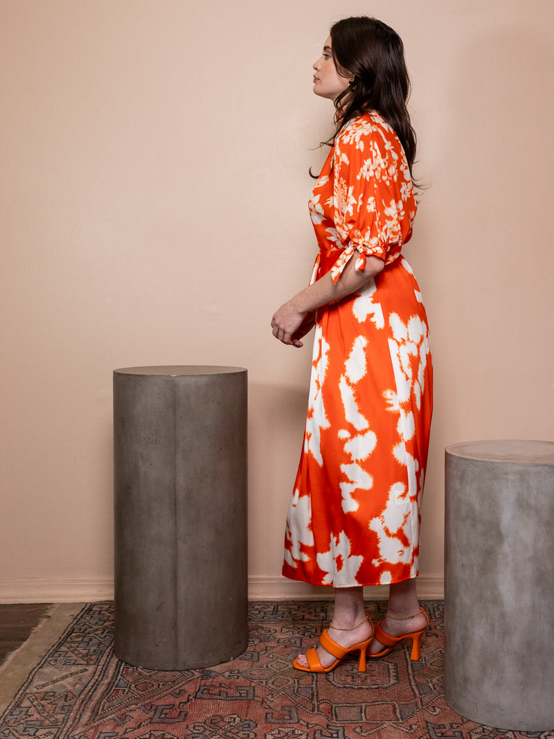 Woman wearing orange skirt and top with white pattern against pink background.