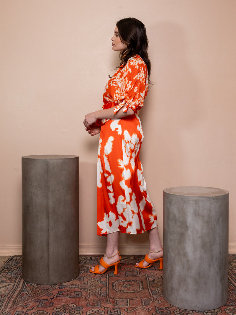 Woman wearing orange skirt with white pattern and matching top against pink background