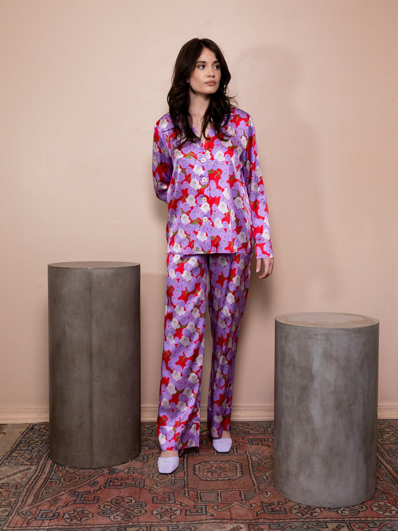 Woman wearing purple and red floral satin top with matching pants against pink background