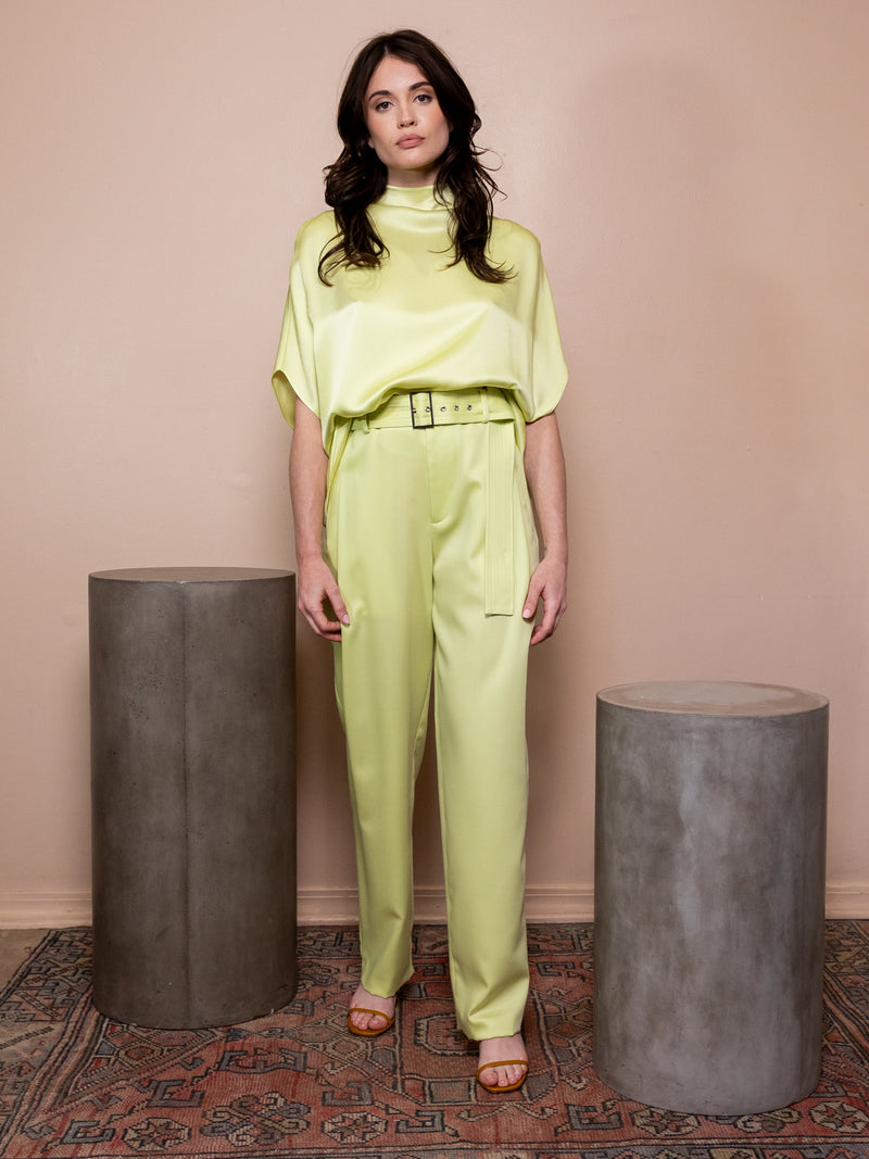 Woman wearing satin green shirt and matching pants against pink background.