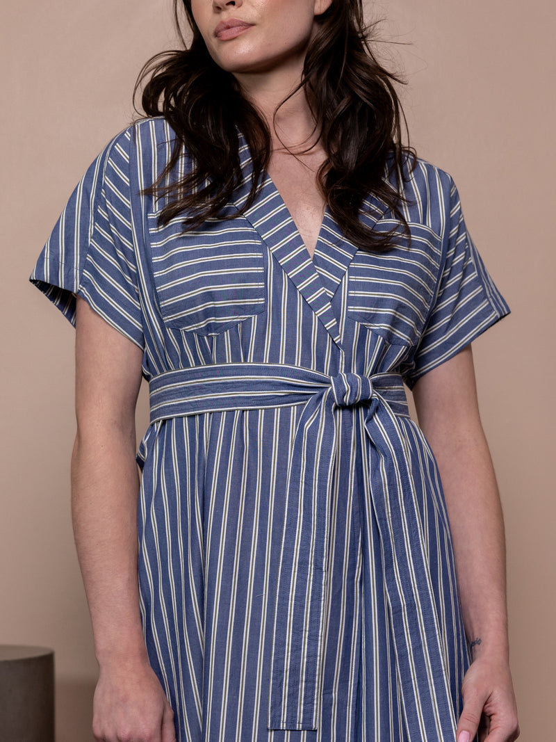 Woman wearing blue striped belted dress against pink background.
