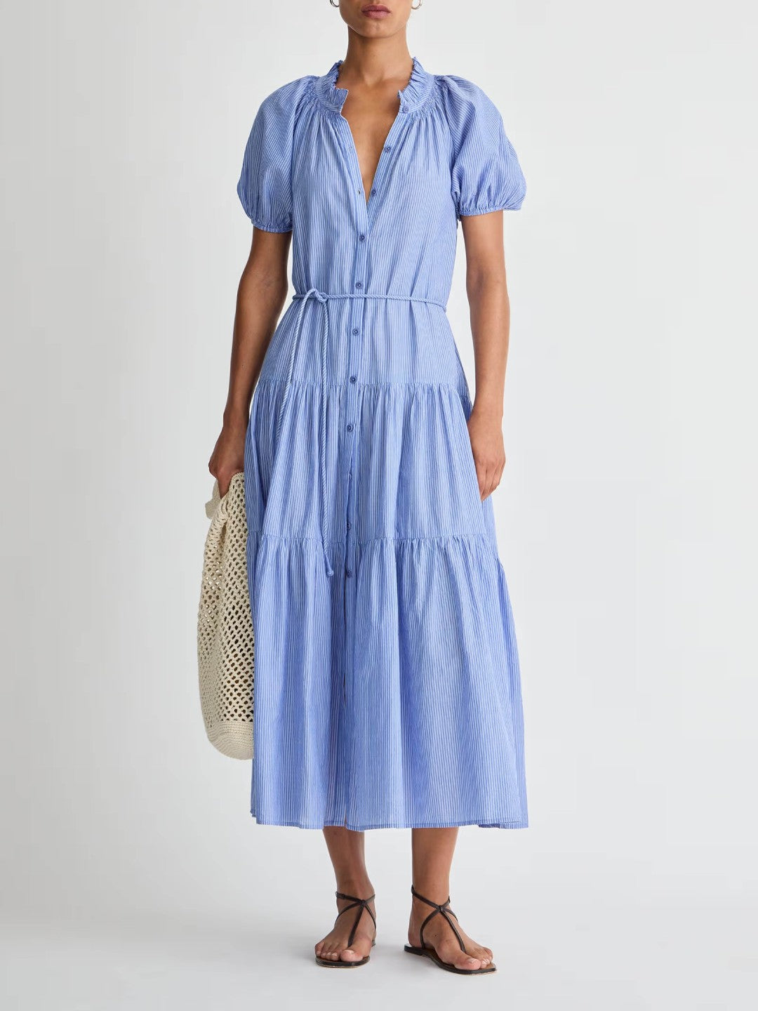 Woman wearing a blue dress holding a woven bag on a plain background