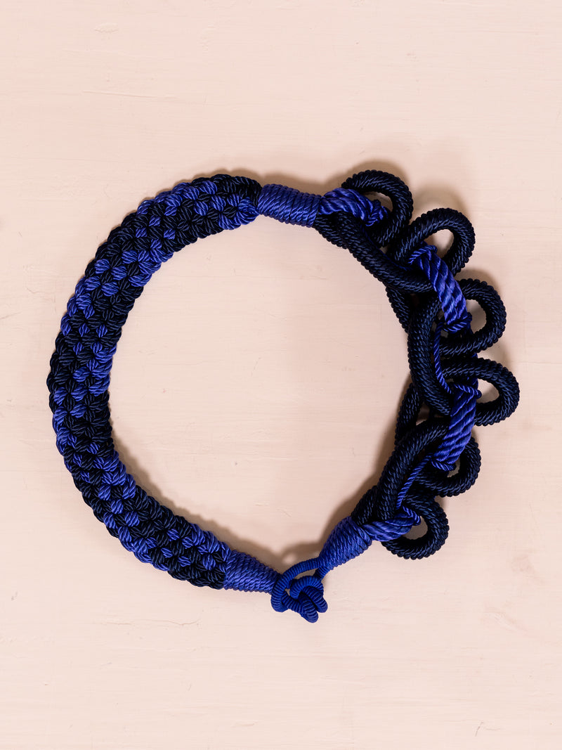 Blue and black woven belt against pink background