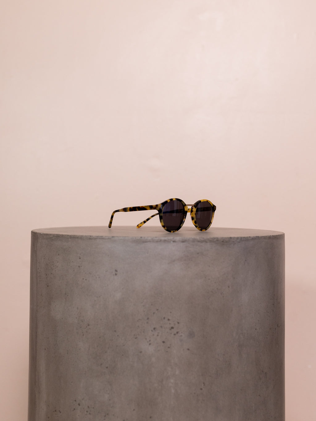 Tortoiseshell sunglasses on pedestal against pink background.