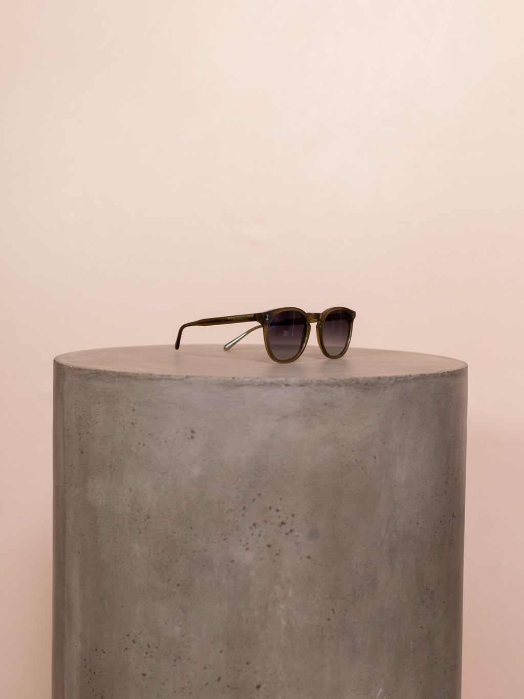 Green round sunglasses on pedestal against pink background.
