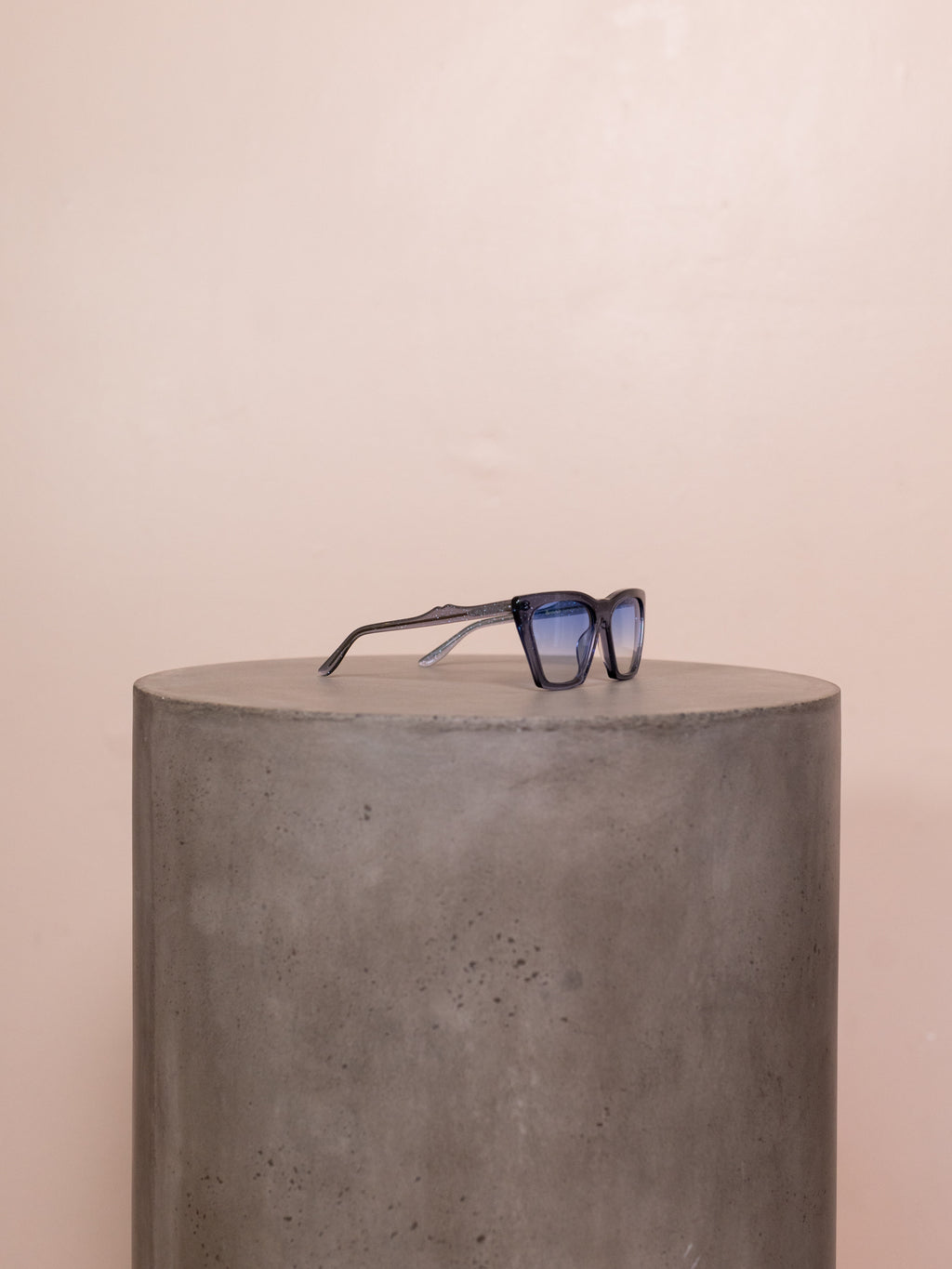 Blue angular sunglasses on pedestal against pink background