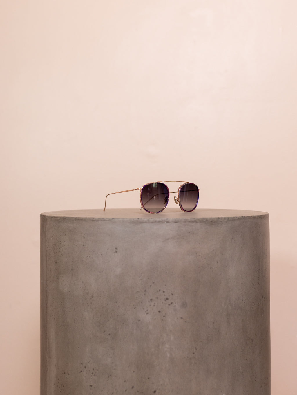 Wire framed sunglasses on pedestal against pink background