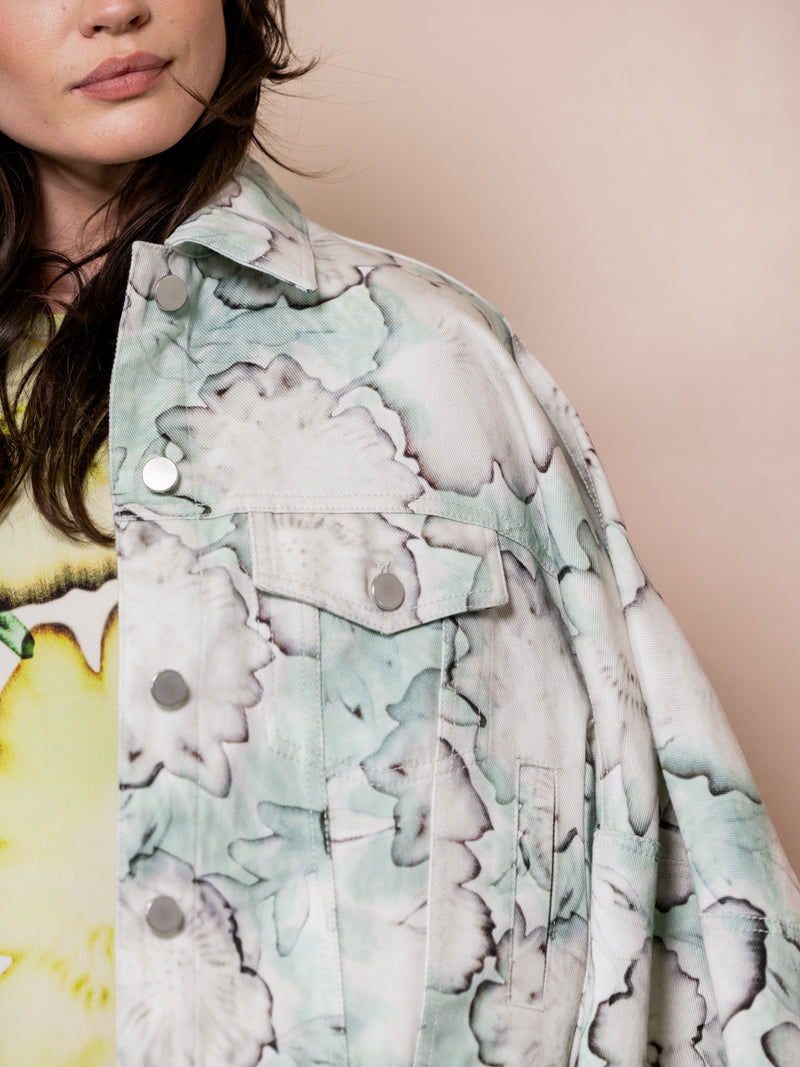 Woman wearing blue floral denim jacket and green floral dress against pink background