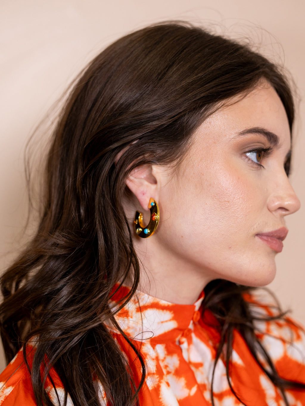 Woman wearing gold hoops with inlaid jewels.