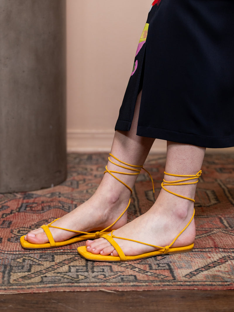 Woman wearing yellow suede tied sandals.