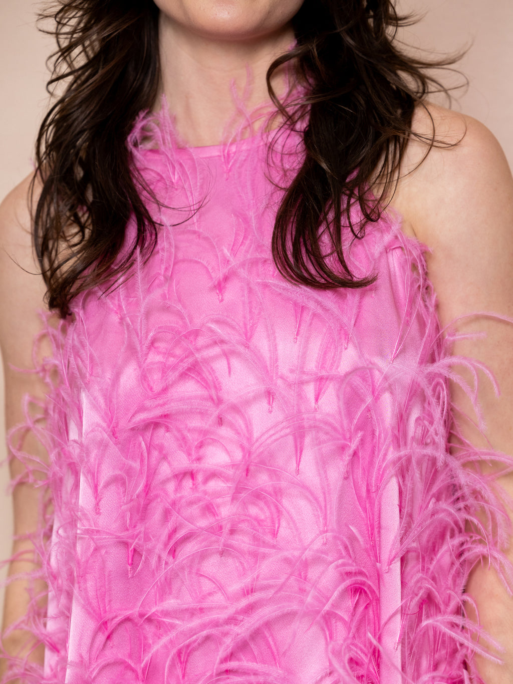 Woman wearing pink mini dress covered in feathers against pink background
