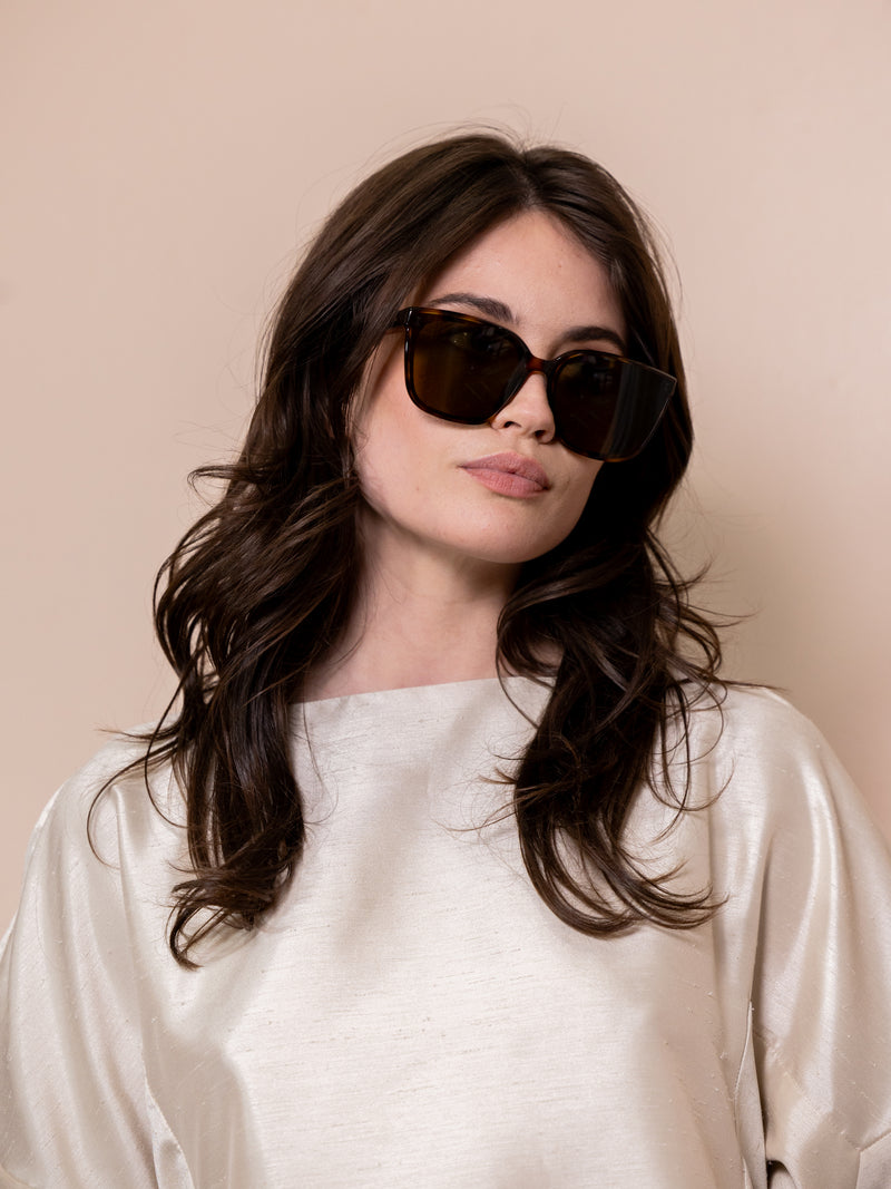 Woman wearing dark brown sunglasses against pink background.