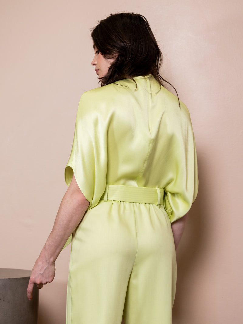 Woman wearing satin green pants and matching top against pink background.