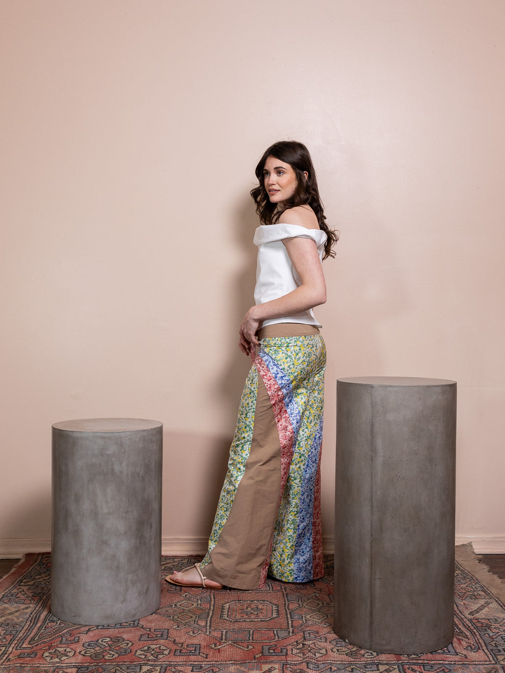 Woman in white top and floral pants against pink background