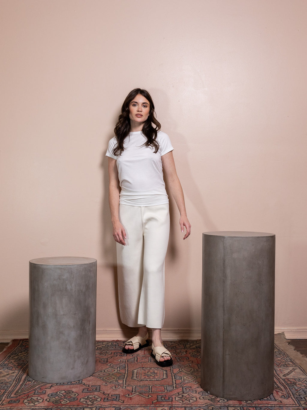 Woman in white top and white pants against pink background