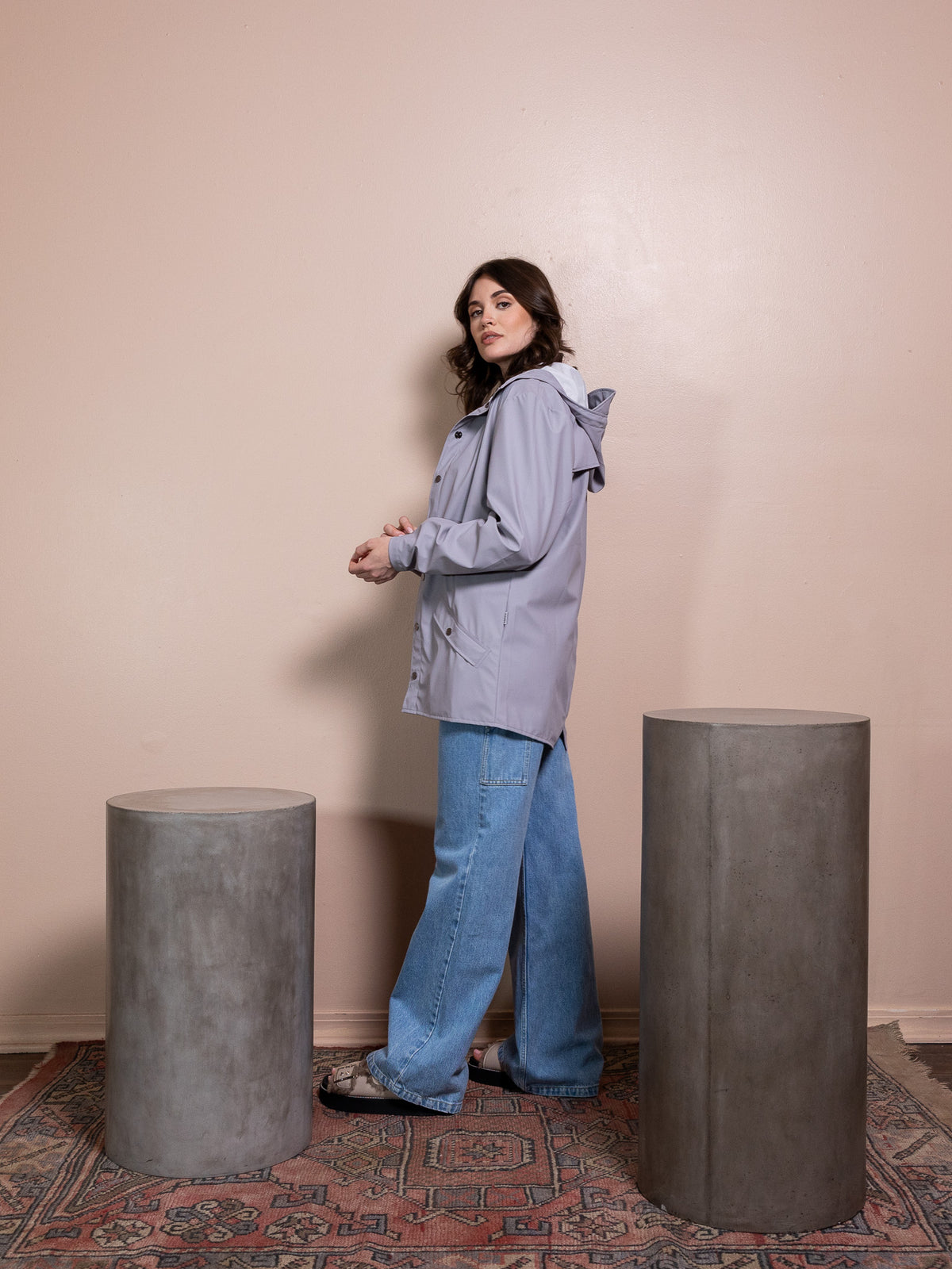 Woman in purple rain jacket and blue jeans against pink background
