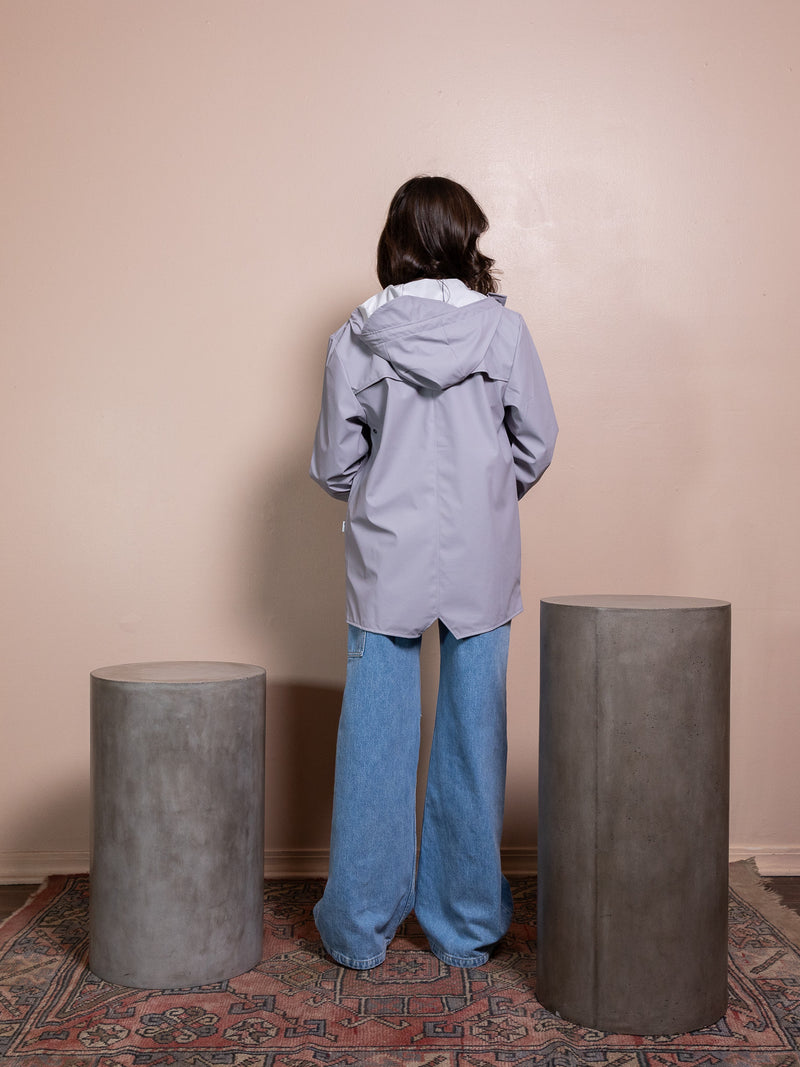 Woman in purple rain jacket and blue jeans against pink background