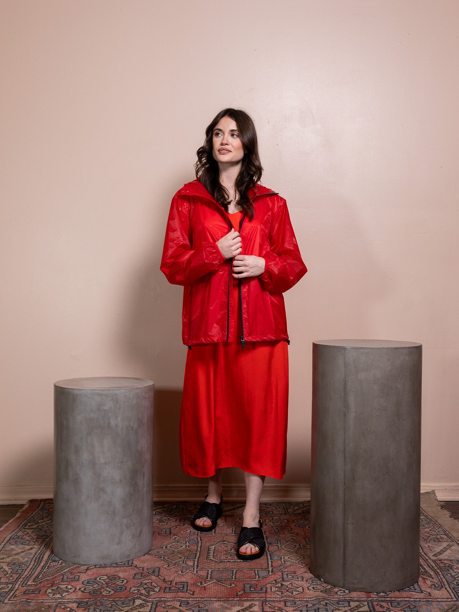 Woman in red dress and red rain jacket against pink background