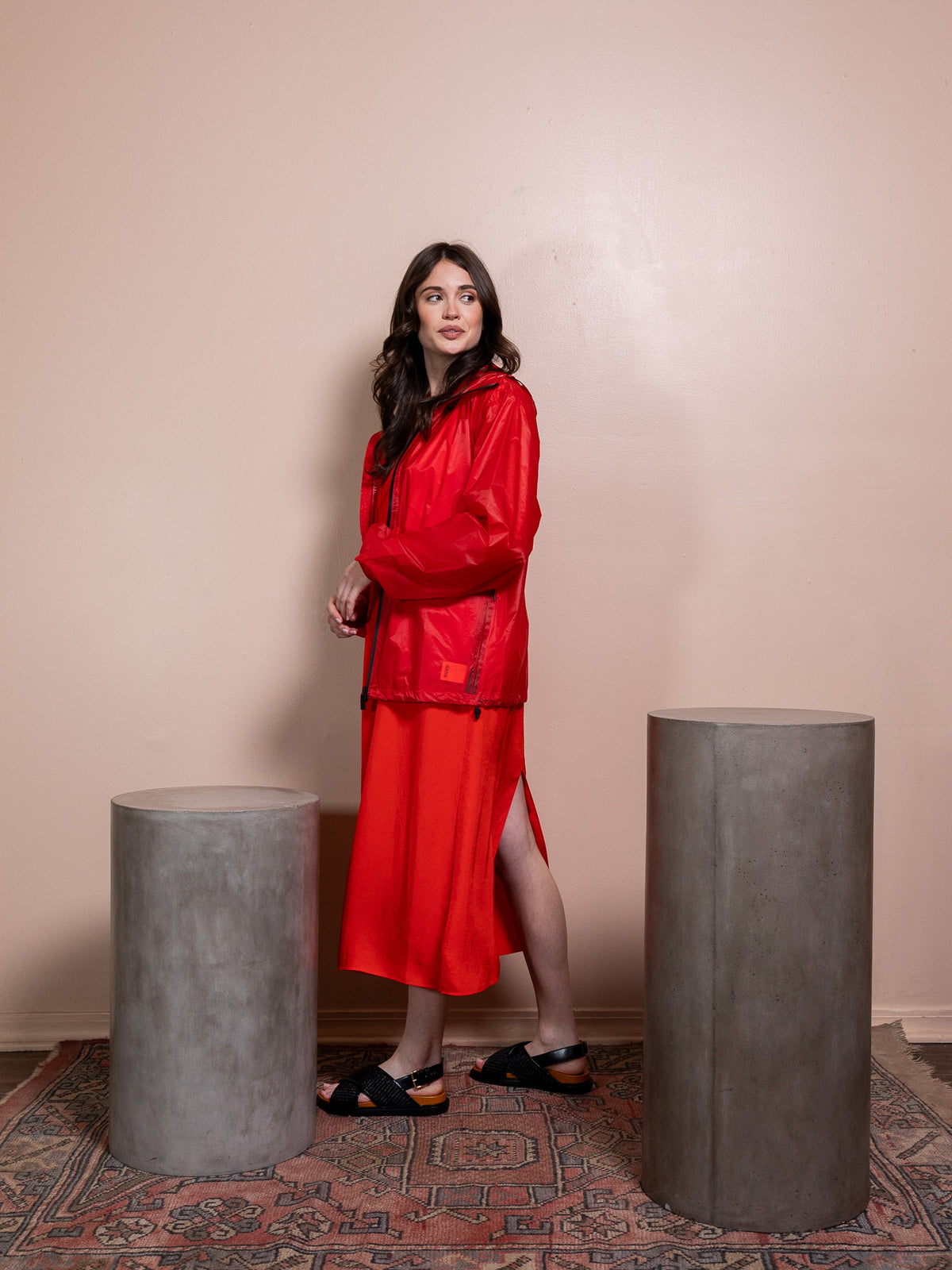 Woman in red dress and red rain jacket against pink background