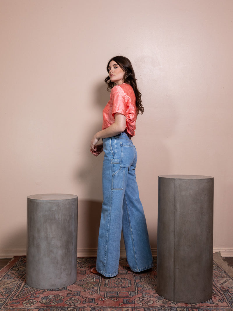 Woman in pink top and blue jeans against pink background
