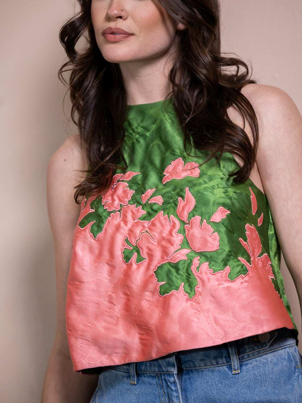 Woman in pink and green floral tank top and blue jeans against pink background