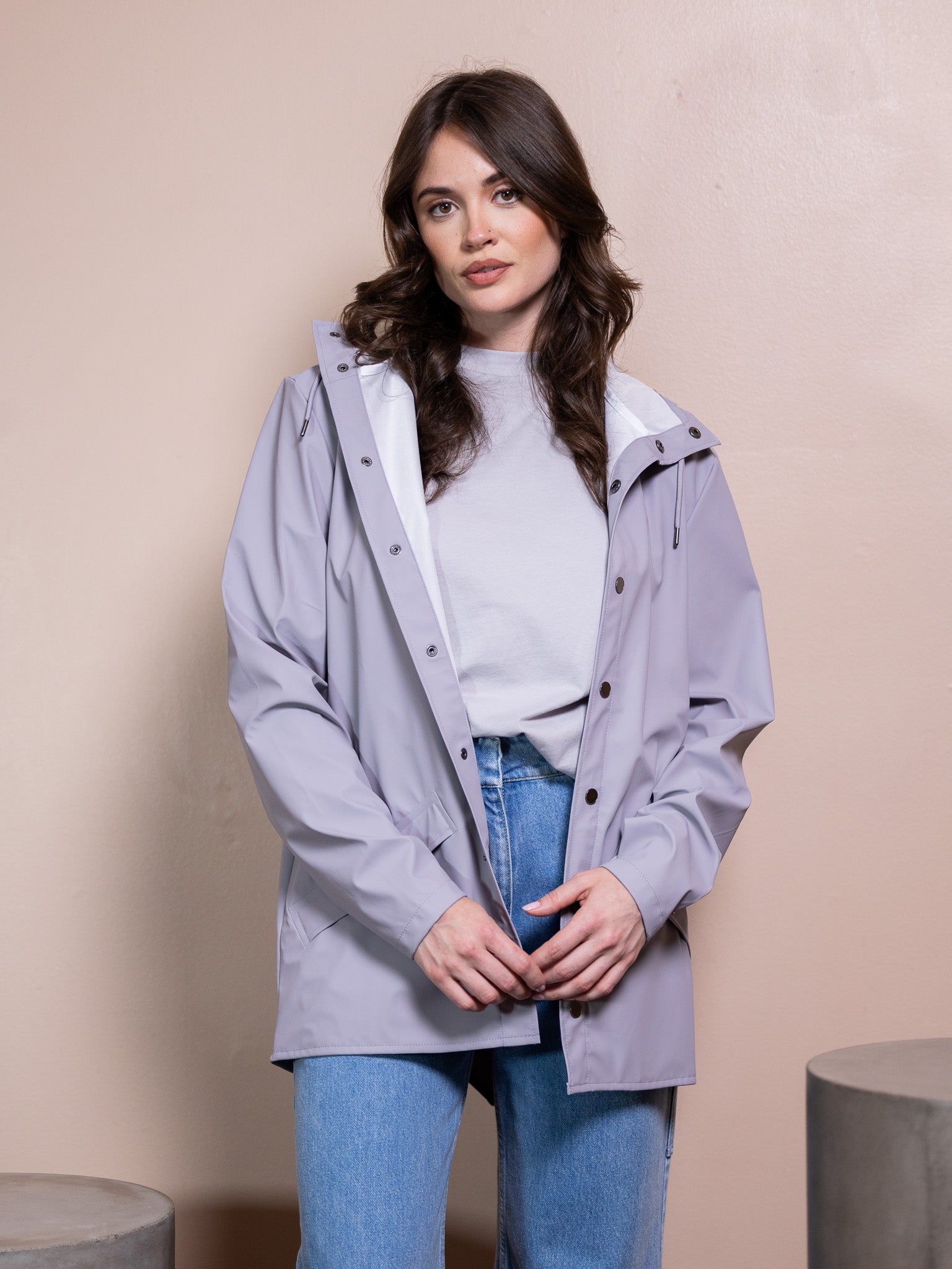 Woman in purple rain jacket and blue jeans against pink background