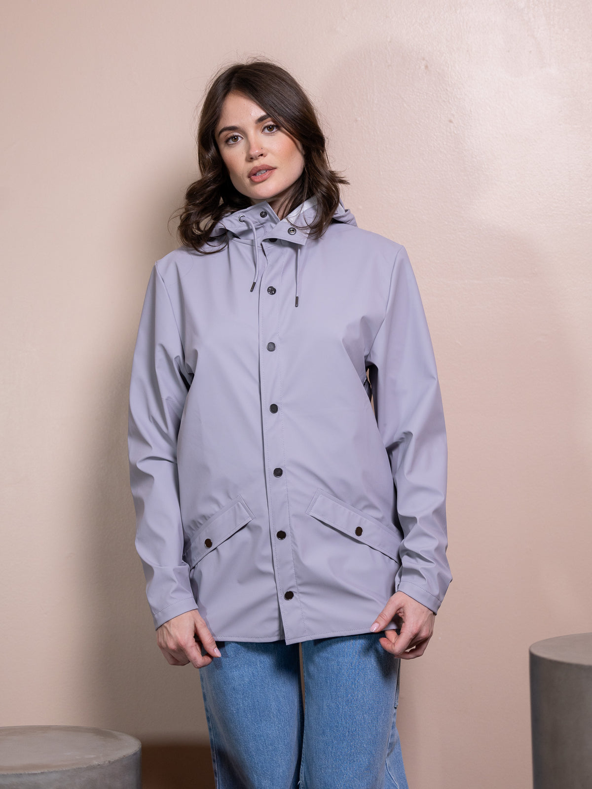 Woman in purple rain jacket and blue jeans against pink background