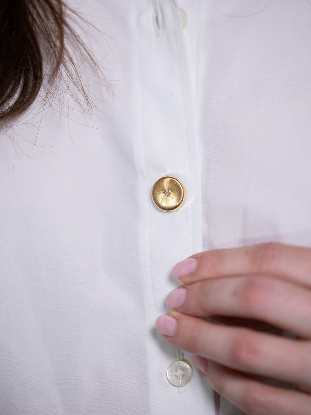 Gold button cover with single diamond on white shirt.