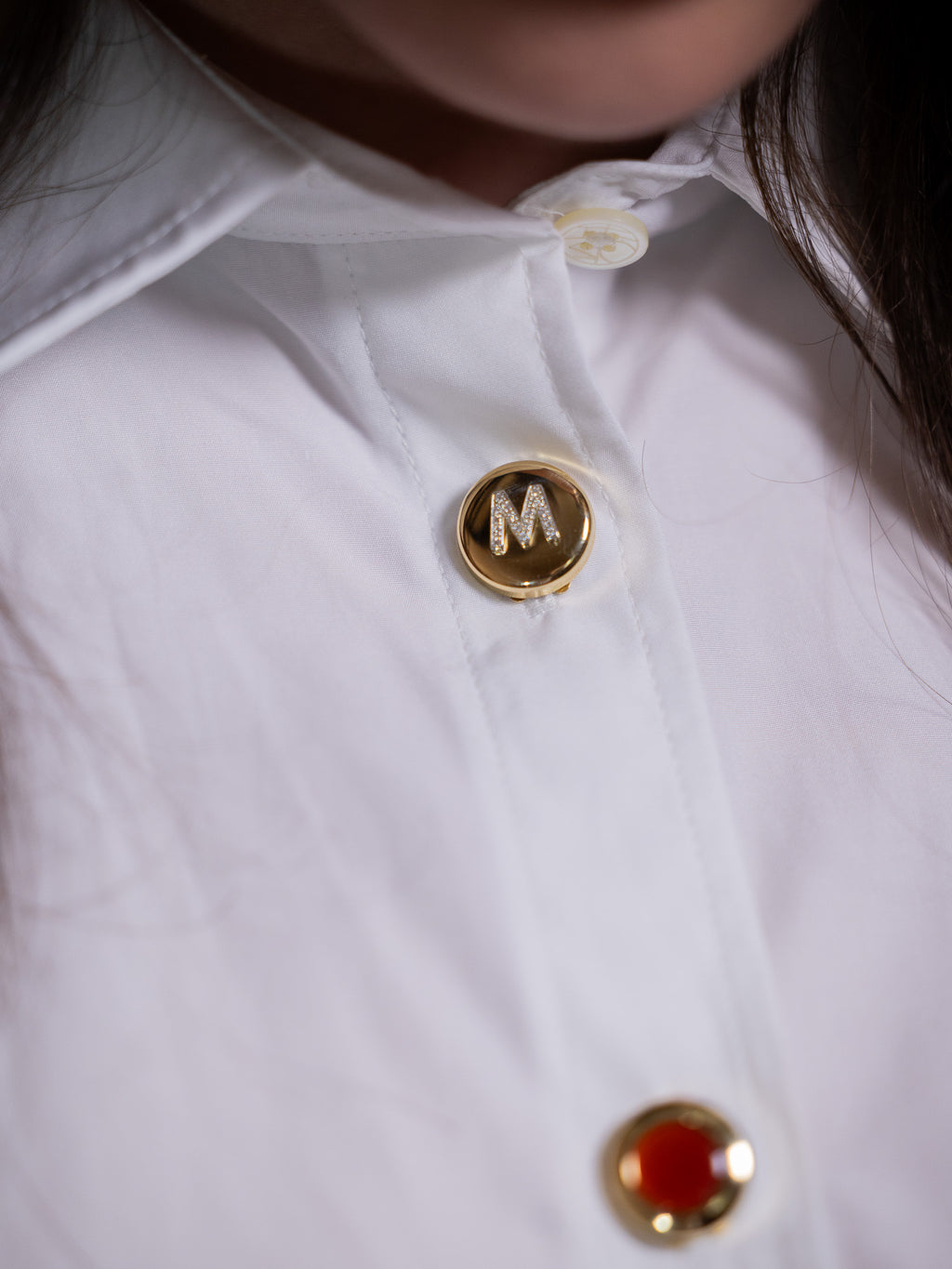 Gold button cover with diamond M on white shirt.