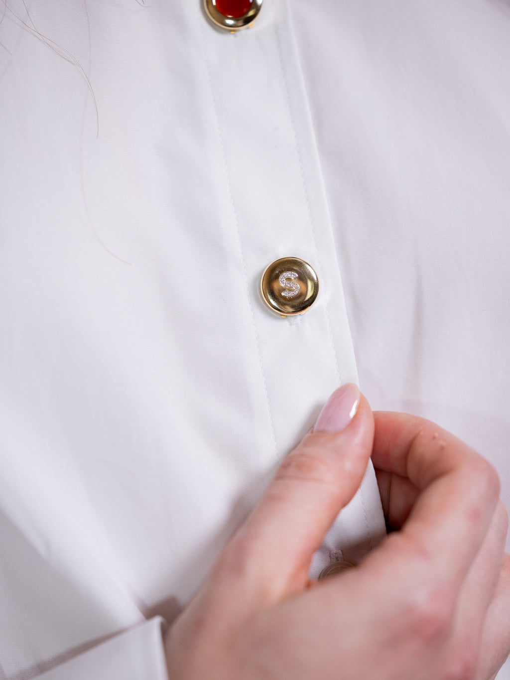 Gold button cover with diamond S on white shirt.
