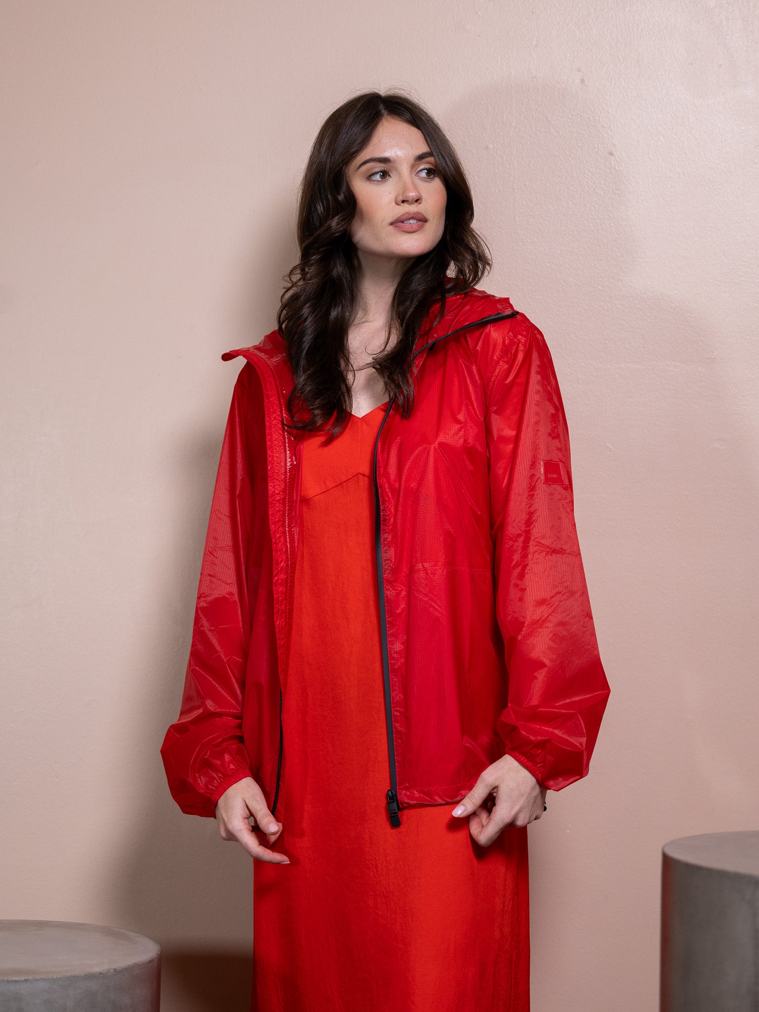 Woman in red dress and red rain jacket against pink background