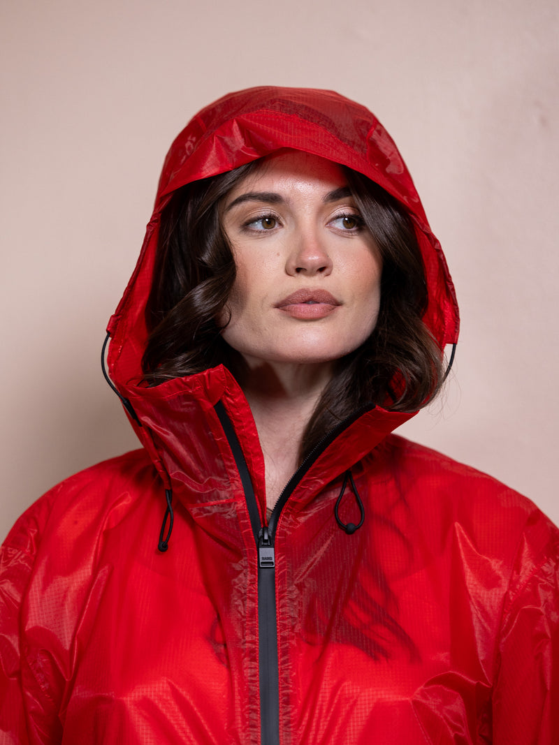 Woman in red dress and red rain jacket against pink background