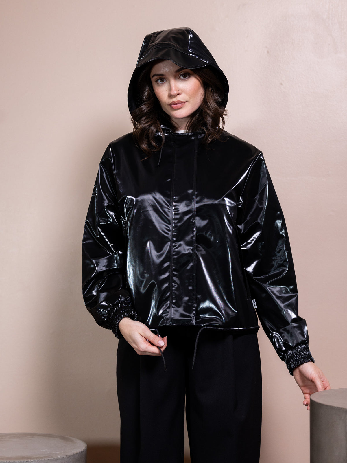 Woman in white top, black rain jacket, and black pants against pink background