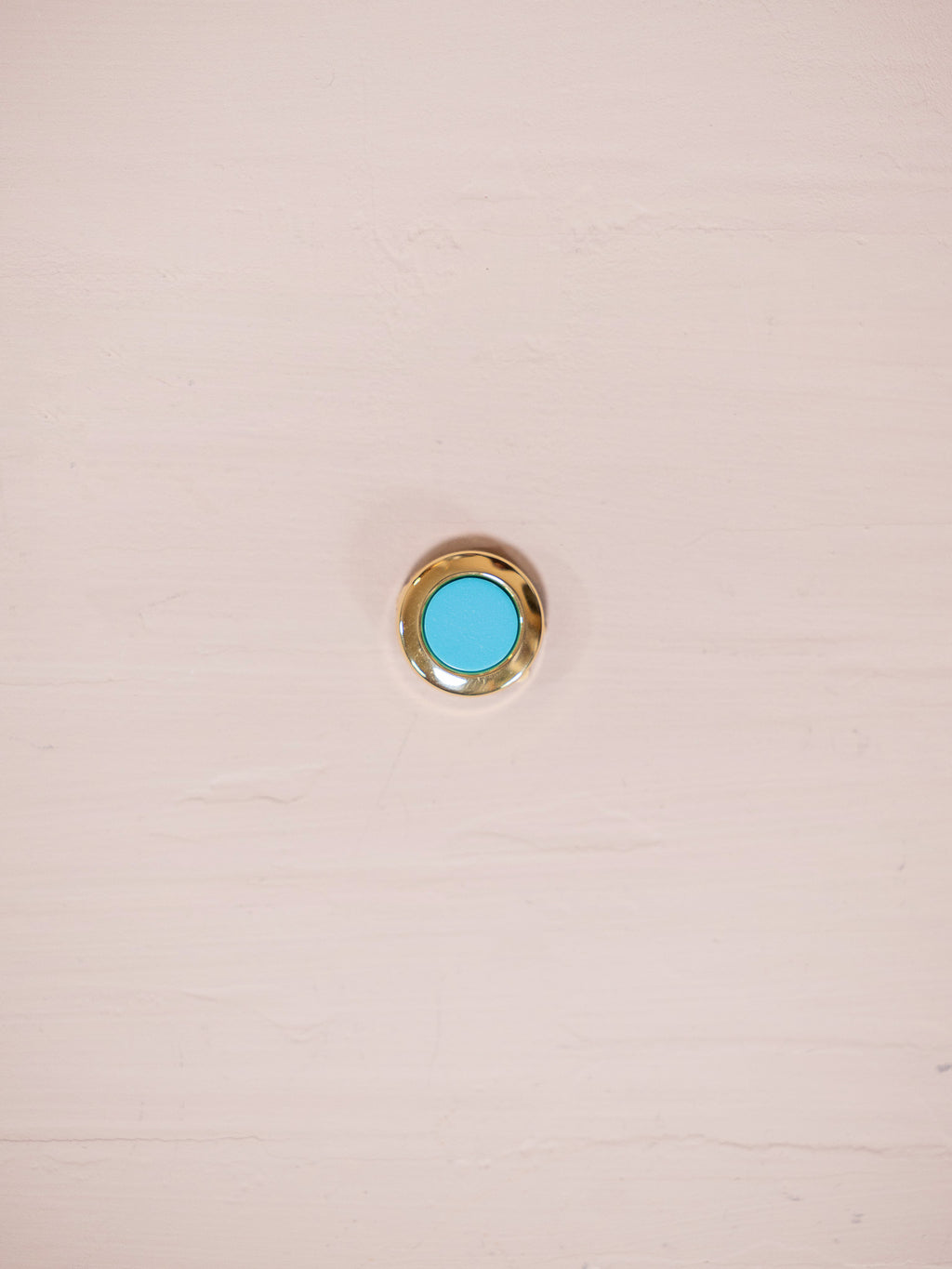 Turquoise and gold button cover on pink background.