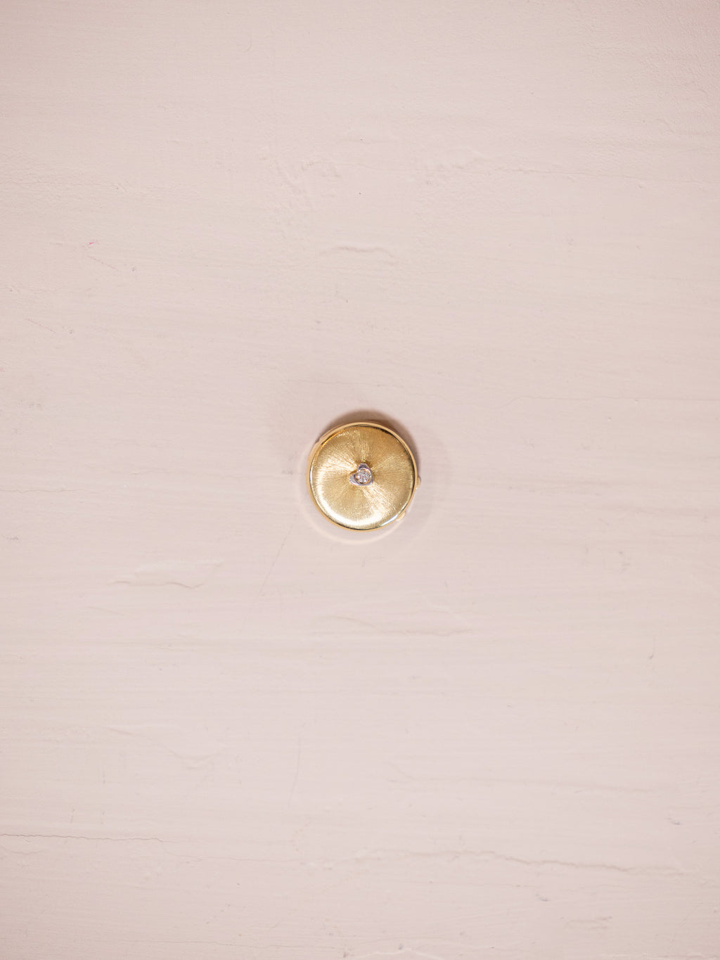 Gold button cover with single diamond on pink background.