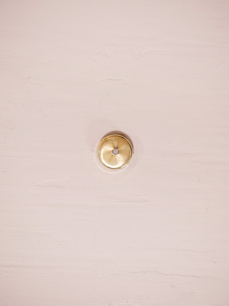 Gold button cover with single diamond on pink background.