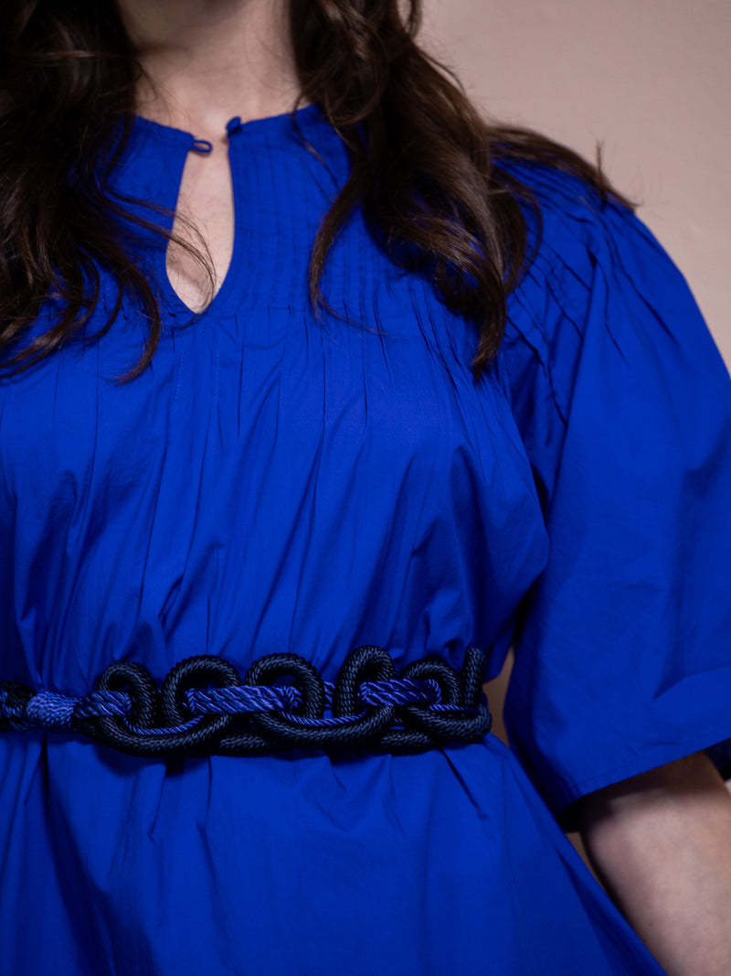 Woman wearing blue dress and a blue and black woven belt.