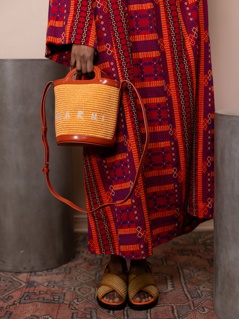 Woman in red dress holding orange bucket bag.