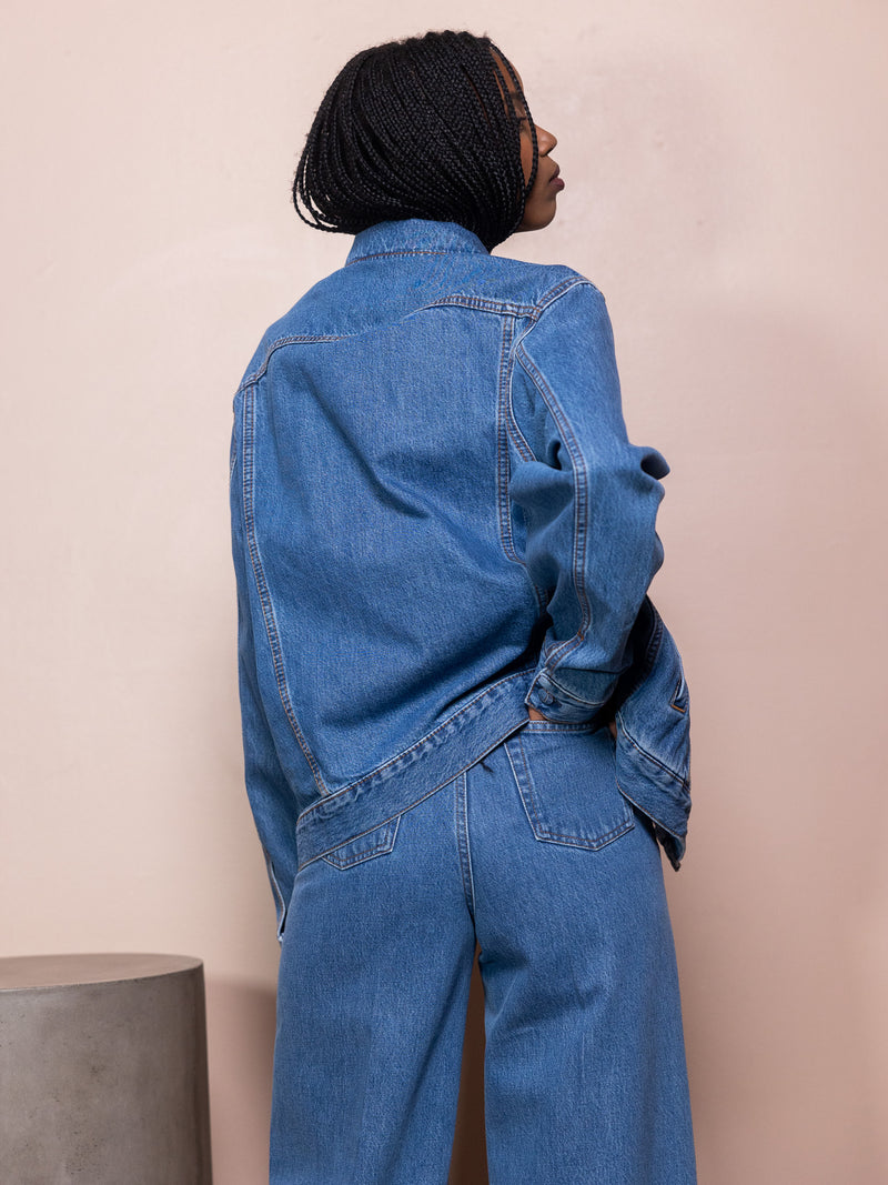 Woman in jean jacket and blue jeans against pink background