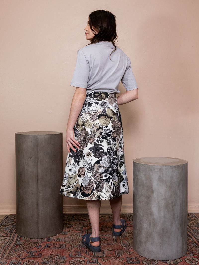 Woman in gray shirt and floral skirt against pink background