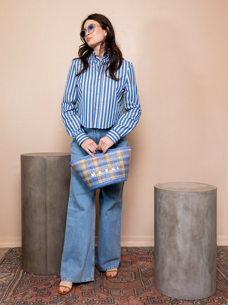 Woman wearing striped shirt and blue jeans holding blue plaid bag.