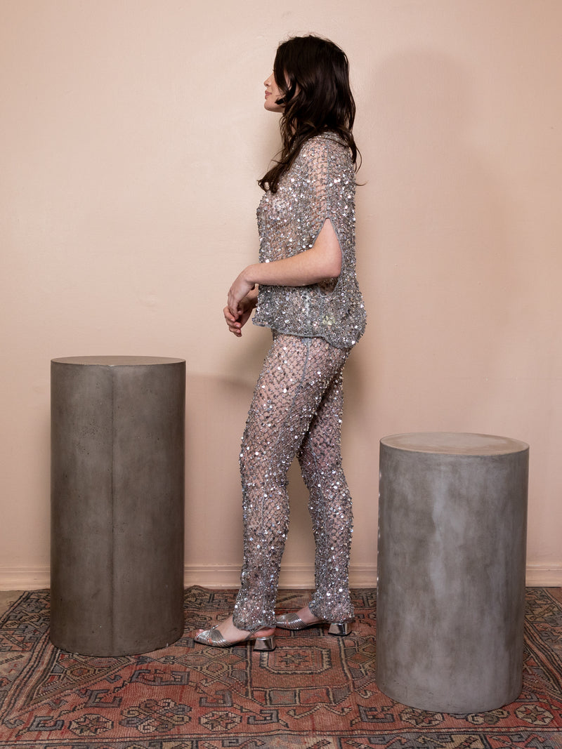 Woman wearing silver sequin pants and matching top against pink background.